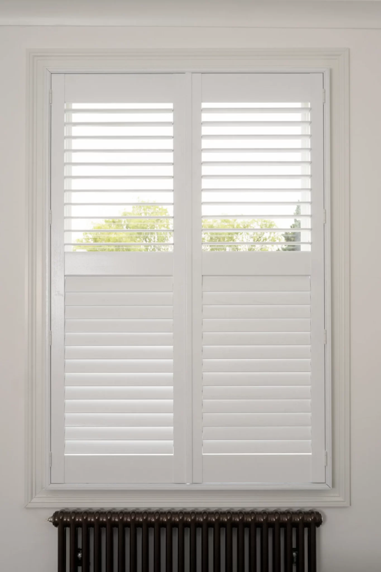 White full-height plantation shutters with a mid-rail fitted to a sash window above a period radiator
