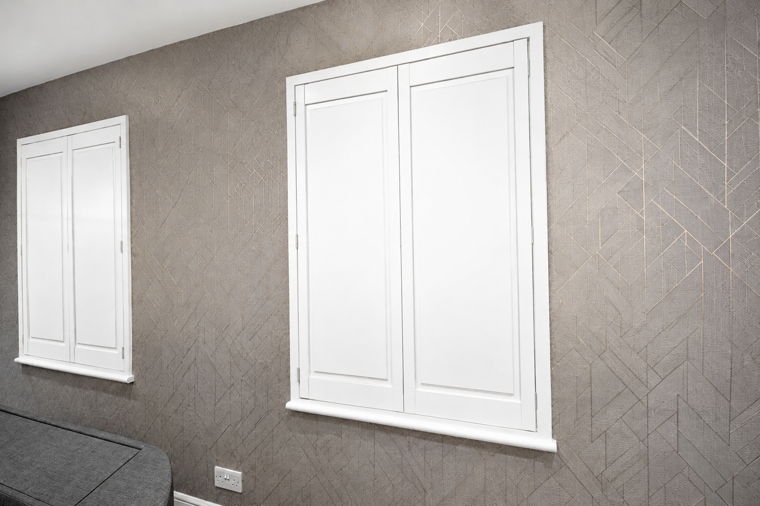 White full panel solid shutters closed across two bedroom windows with textured grey wallpaper