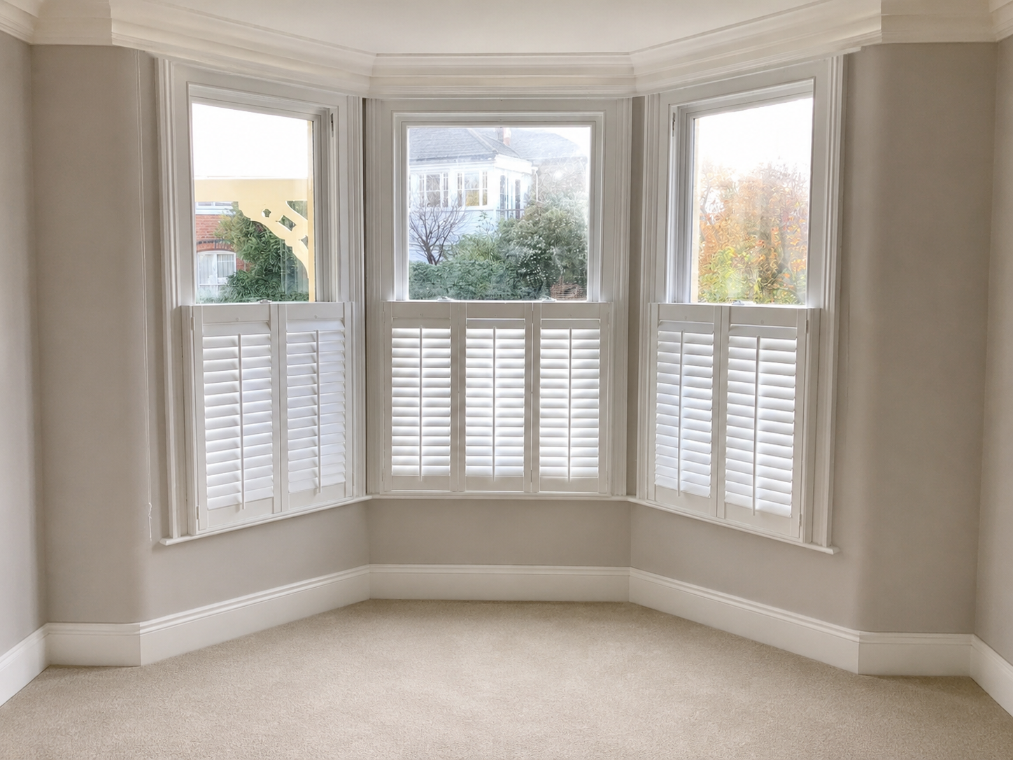 White café-style plantation shutters fitted to a three-facet bay window in a neutral bedroom